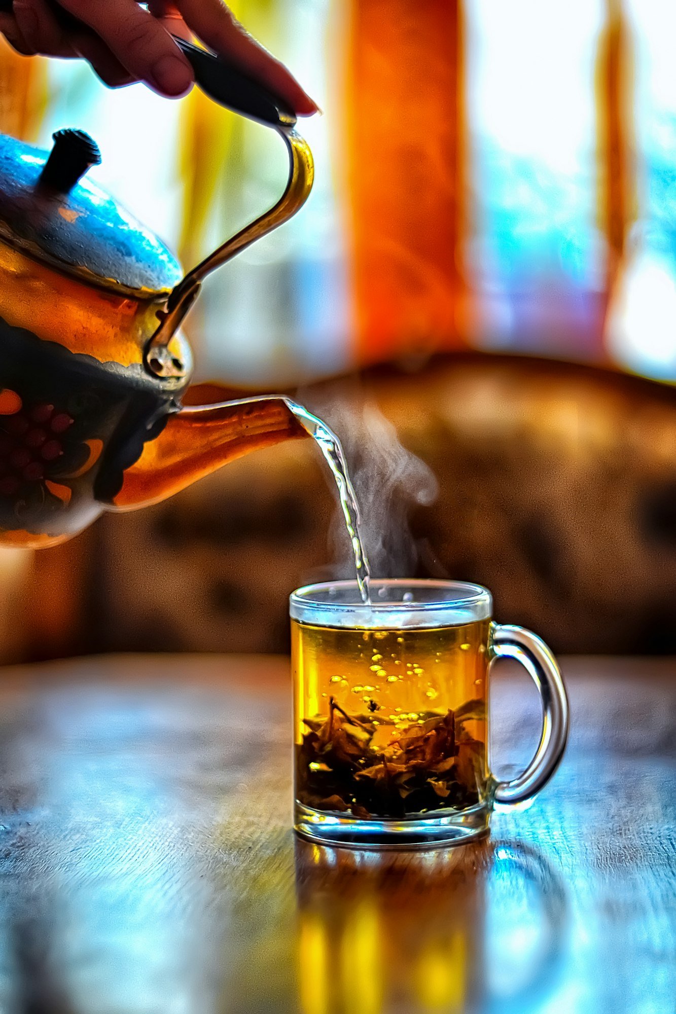 Tea is poured from a teapot into a glass mug. Steam